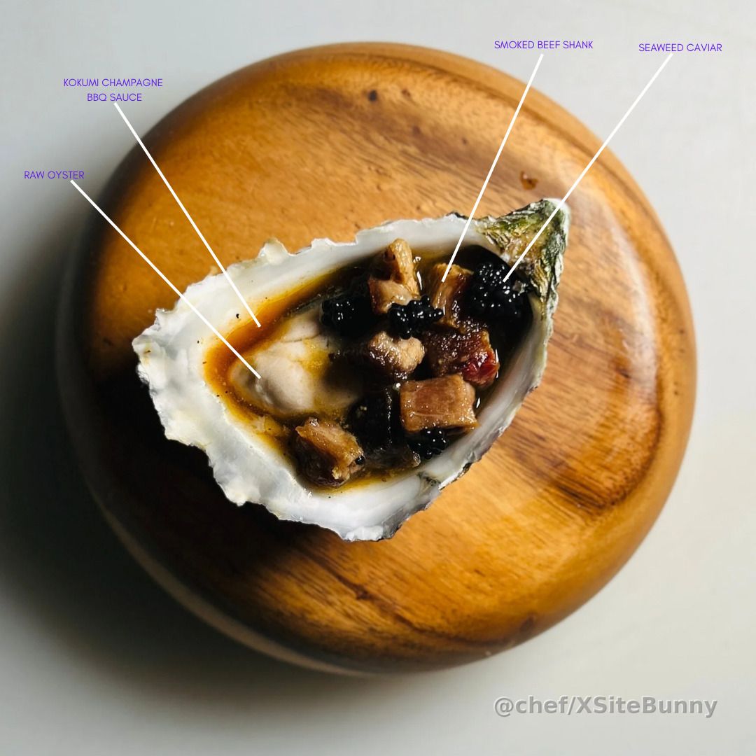 Surf meets smoke in one briny, bold bite.

A raw oyster layered with smoked beef shank, seaweed caviar, and finished with kokumi champagne BBQ sauce. It’s ocean depth, backyard smoke, and elegant acid all in one shell—unexpected, unapologetic, unforgettable.

